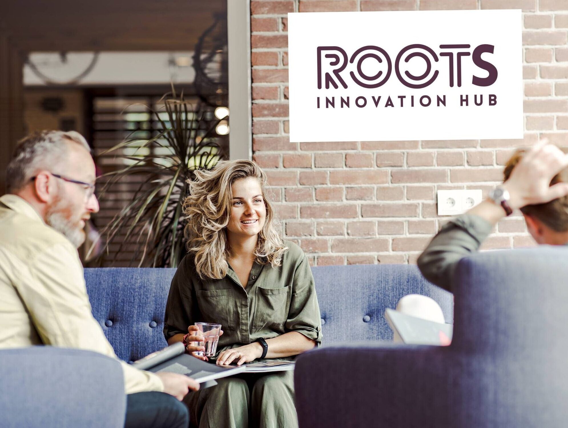 3 personen op sofa's met op de achtergrond een bord met de tekst 'Roots Innovation Hub'