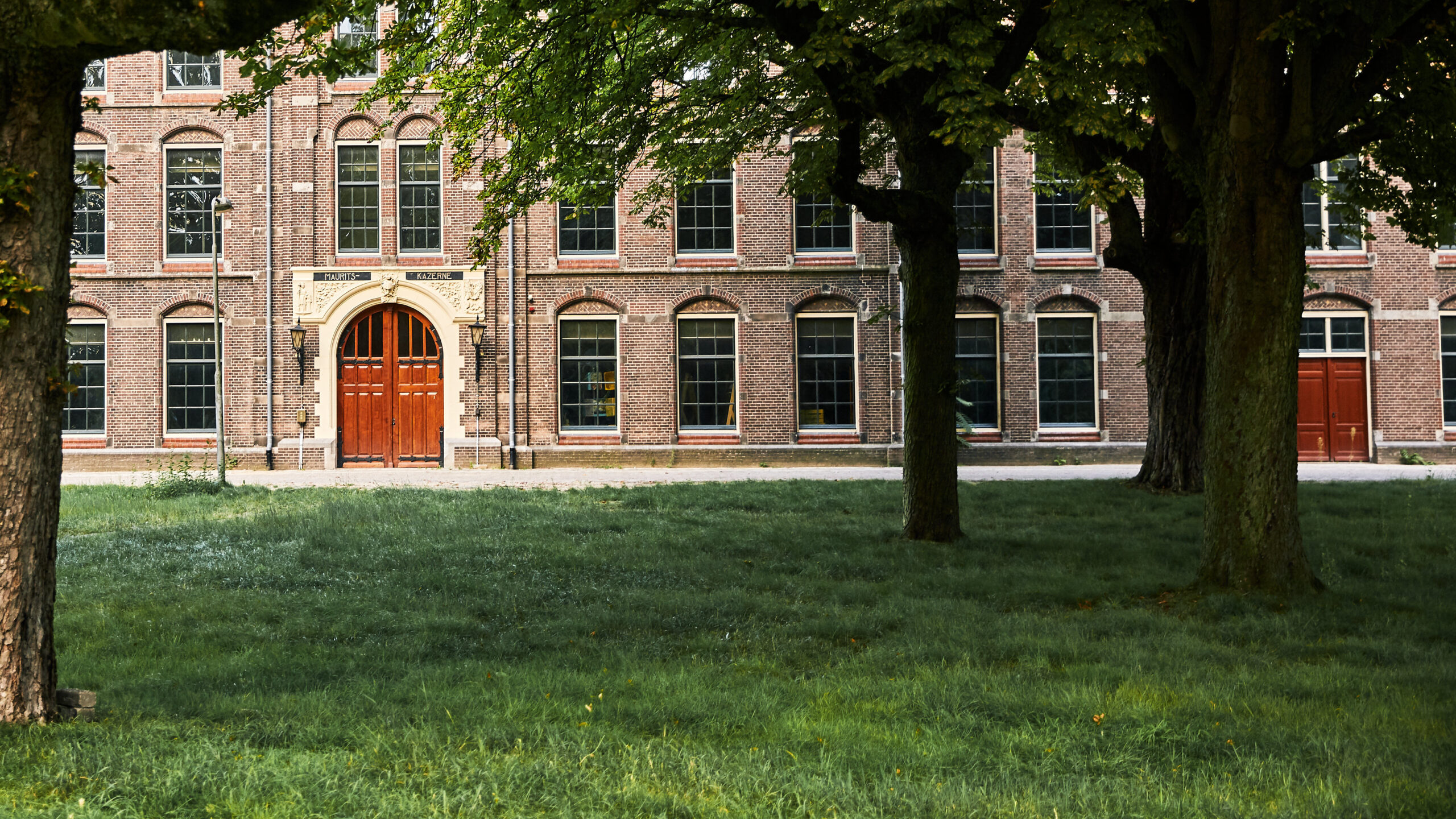 Foto van het gebouw Mauritskazerne met daarvoor het Frisopark met gras en bomen